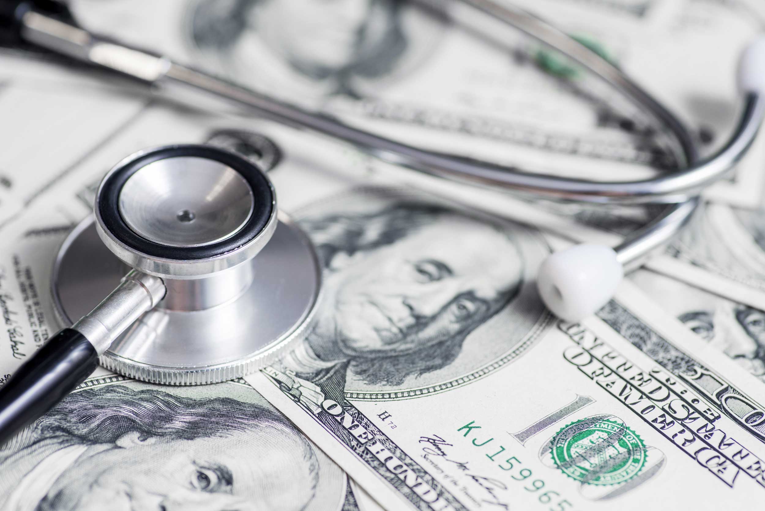 Stethoscope resting on US hundred dollar bills